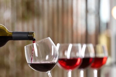 Photo of Pouring red wine from bottle into glass indoors, closeup. Space for text