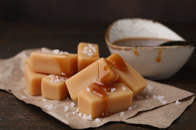 Delicious candies with sea salt and caramel sauce on wooden table, closeup