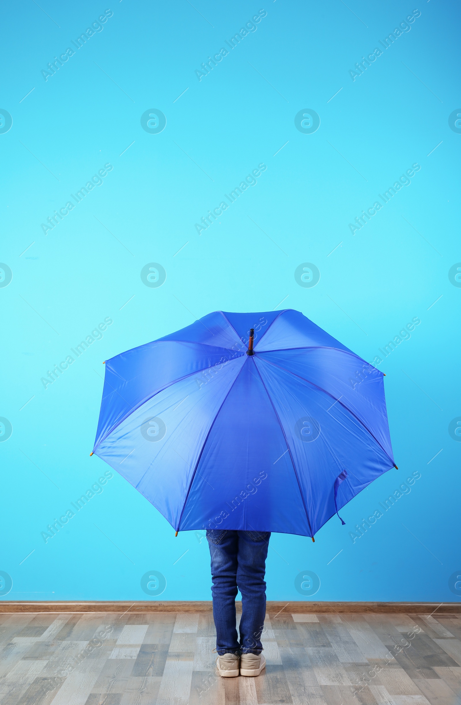 Photo of Little boy with blue umbrella near color wall. Space for text