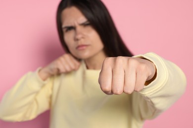 Young woman ready to fight against pink background, focus on hand. Space for text