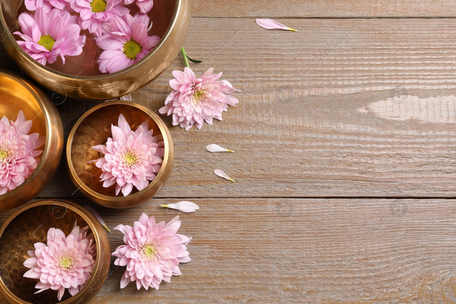 Photo of Tibetan singing bowls with water and beautiful flowers on wooden table, flat lay. Space for text