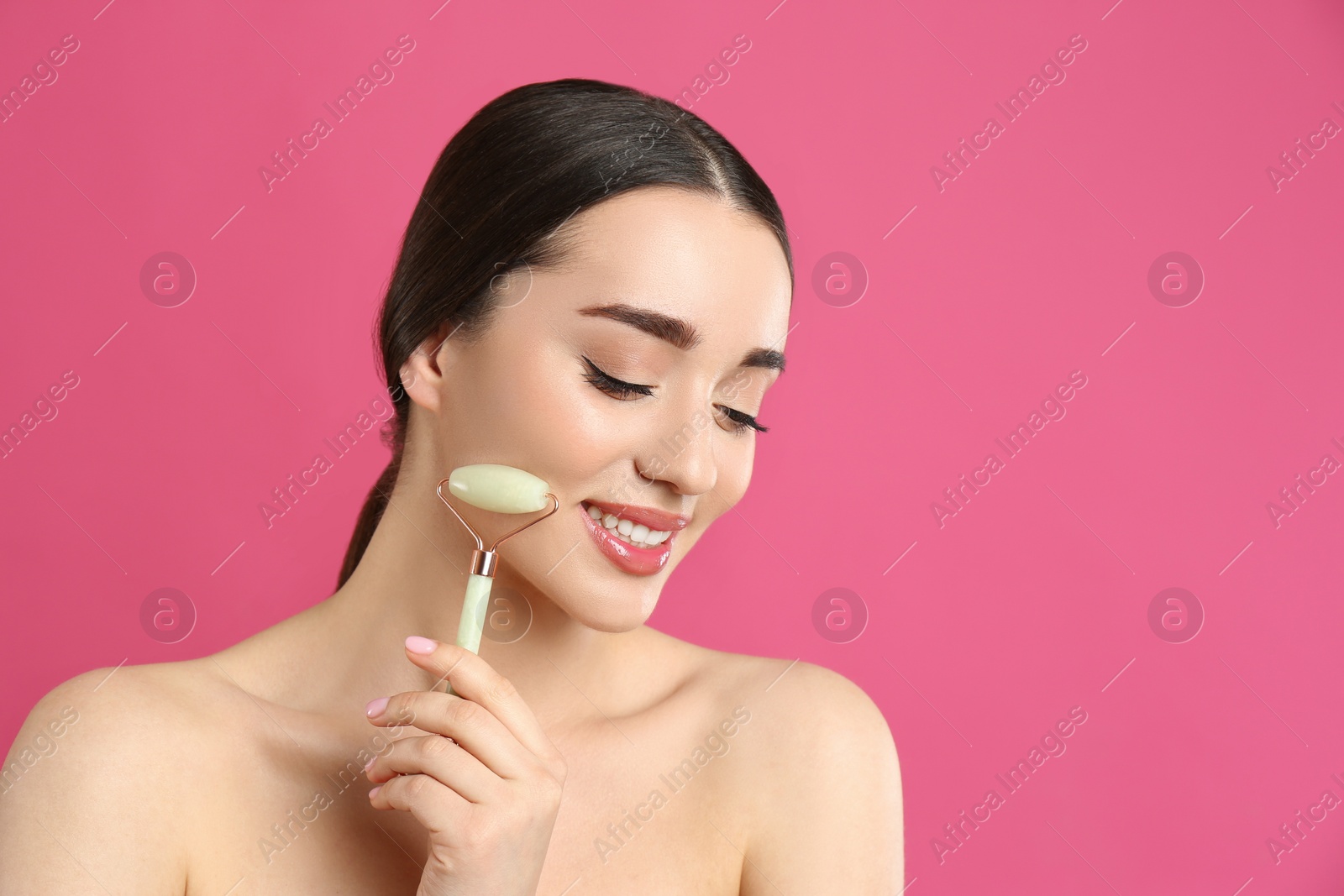 Photo of Woman using natural jade face roller on pink background, space for text