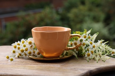 Photo of Cup of delicious chamomile tea and fresh flowers outdoors