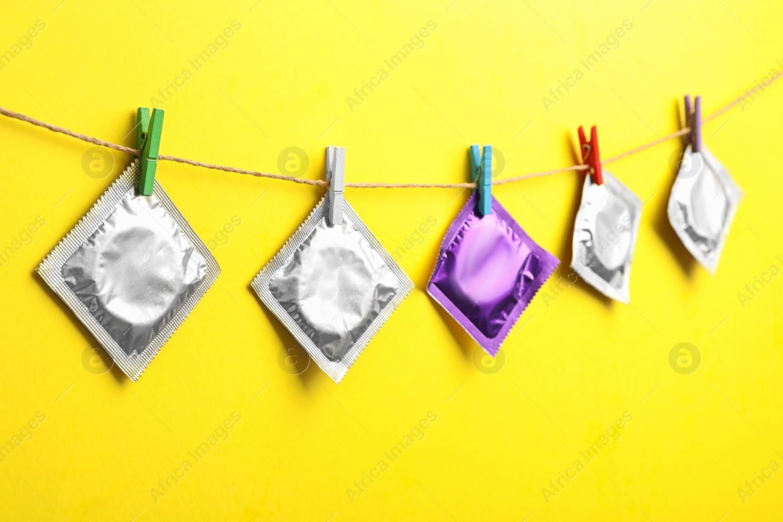 Photo of Colorful condoms hanging on clothesline against yellow background. Safe sex concept