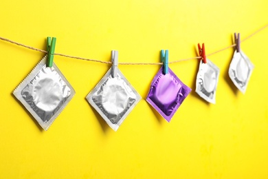 Colorful condoms hanging on clothesline against yellow background. Safe sex concept