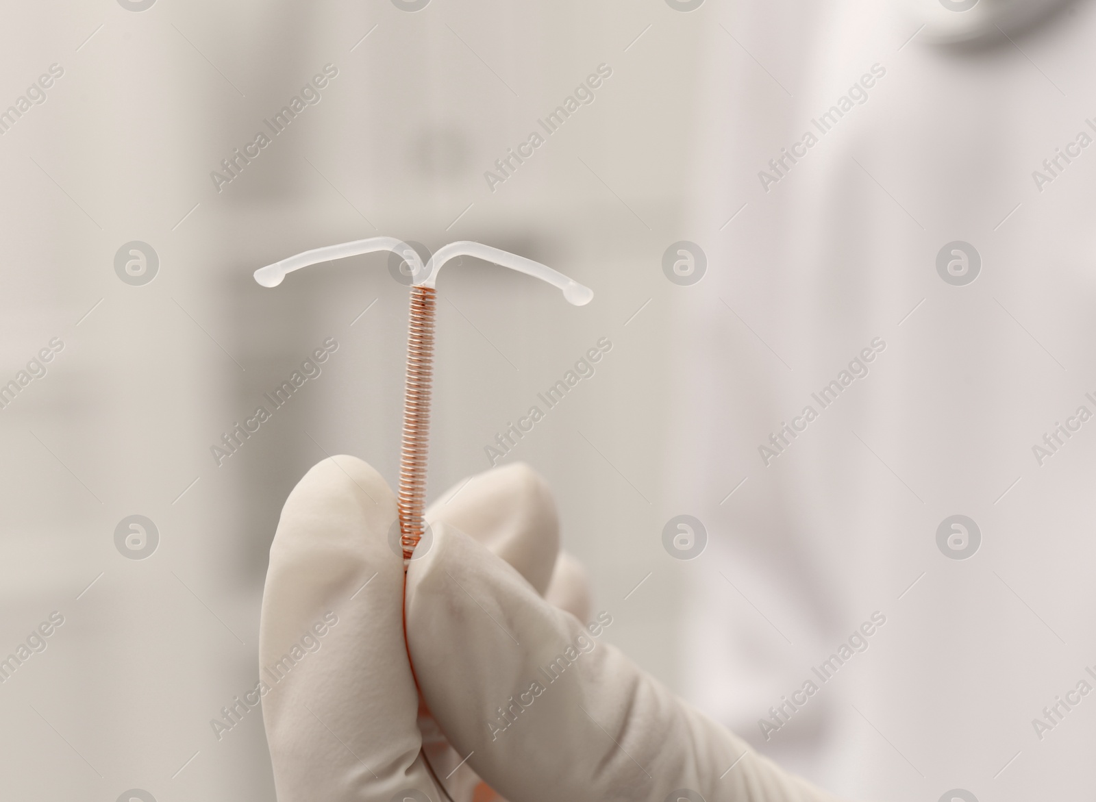 Photo of Doctor holding T-shaped intrauterine birth control device on blurred background, closeup