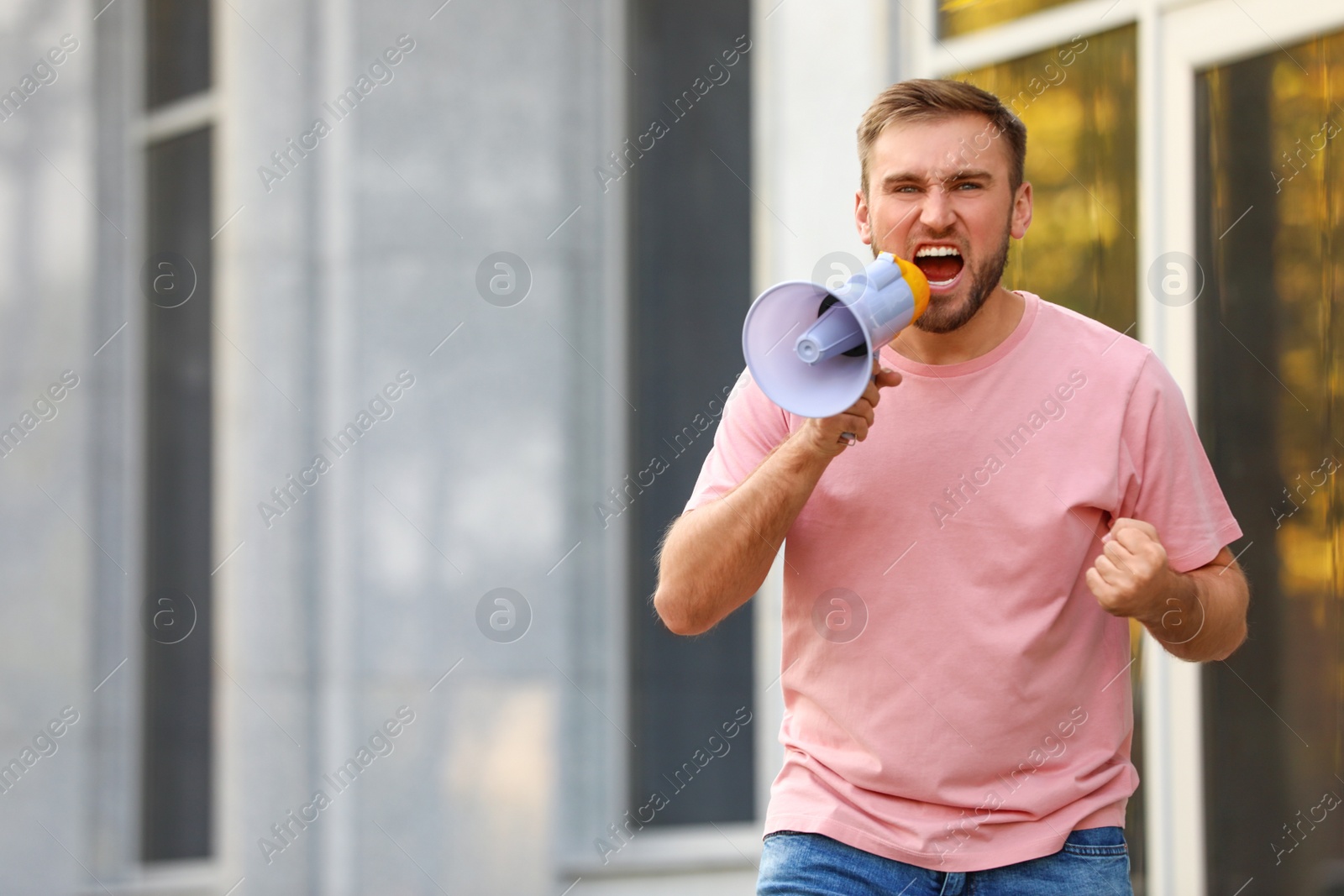 Image of Emotional young man with megaphone outdoors. Protest leader