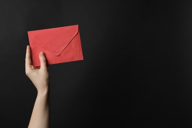 Photo of Woman holding red paper envelope on black background, closeup. Space for text