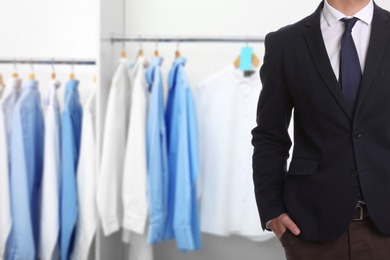 Businessman and rack with clean clothes at dry-cleaner's, closeup. Space for text 