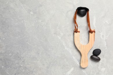 Wooden slingshot with stones on light grey marble background, flat lay. Space for text