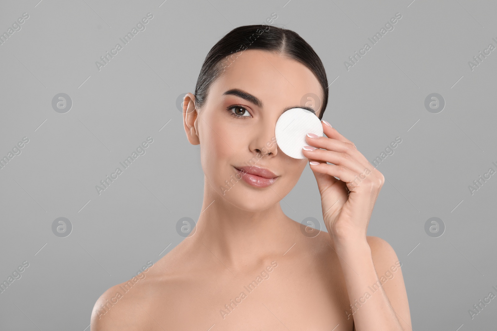 Photo of Beautiful woman removing makeup with cotton pad on light grey background