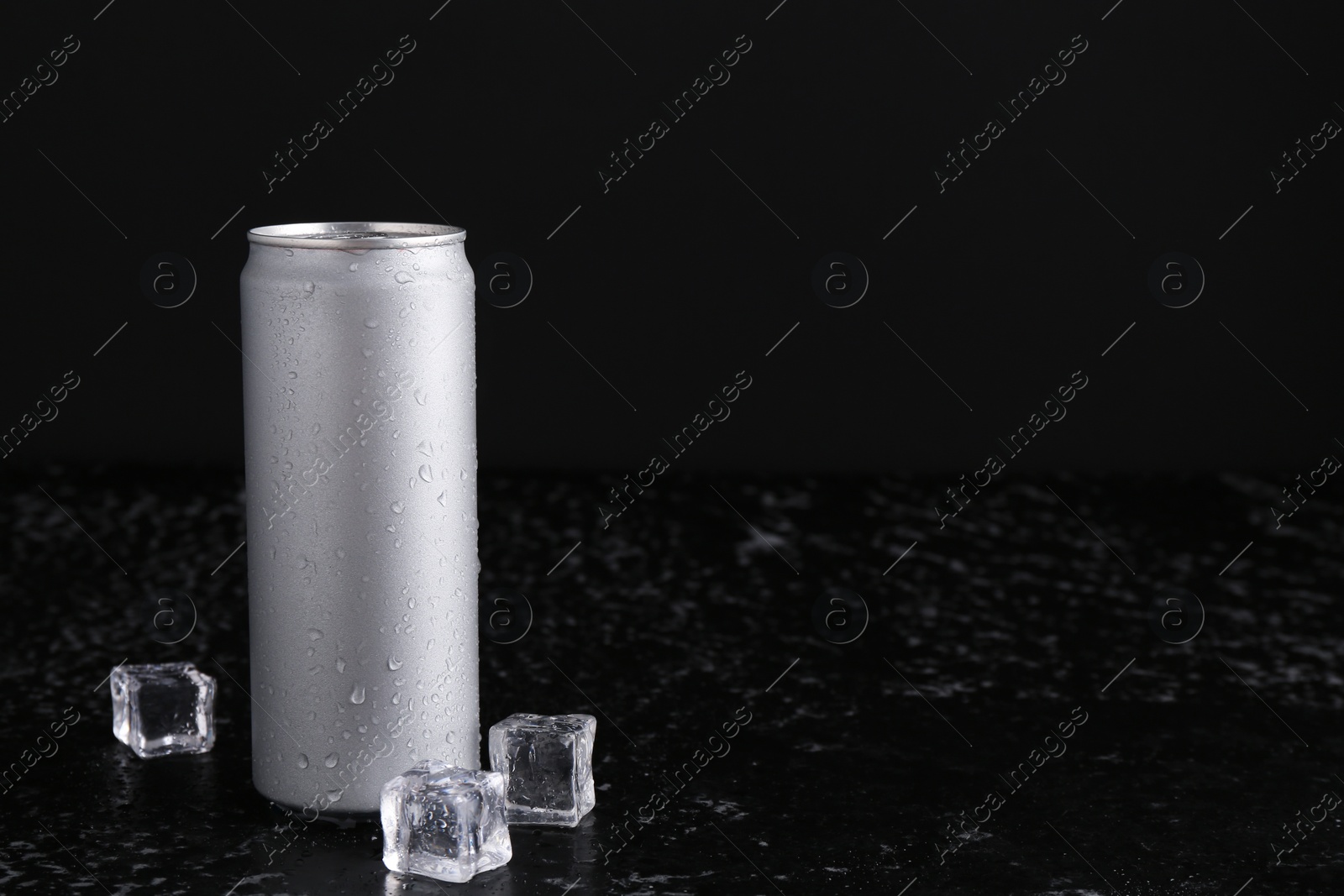 Photo of Energy drink in wet can and ice cubes on black textured table, space for text