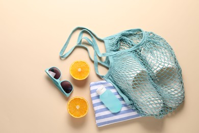 String bag, different beach accessories and orange on beige background, flat lay