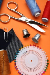 Flat lay composition with thimbles and different sewing tools on orange background