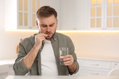 Photo of Man taking pill against migraine in kitchen, space for text