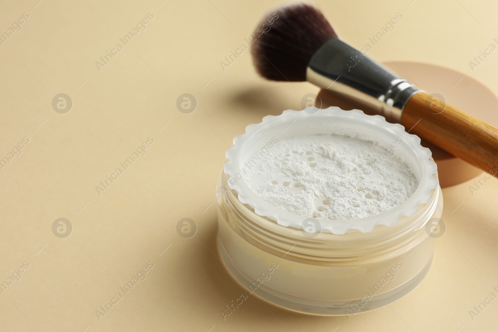 Photo of Rice loose face powder and makeup brush on beige background, closeup. Space for text