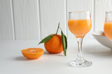 Photo of Tasty tangerine liqueur in glass and fresh citrus fruits on white table. Space for text