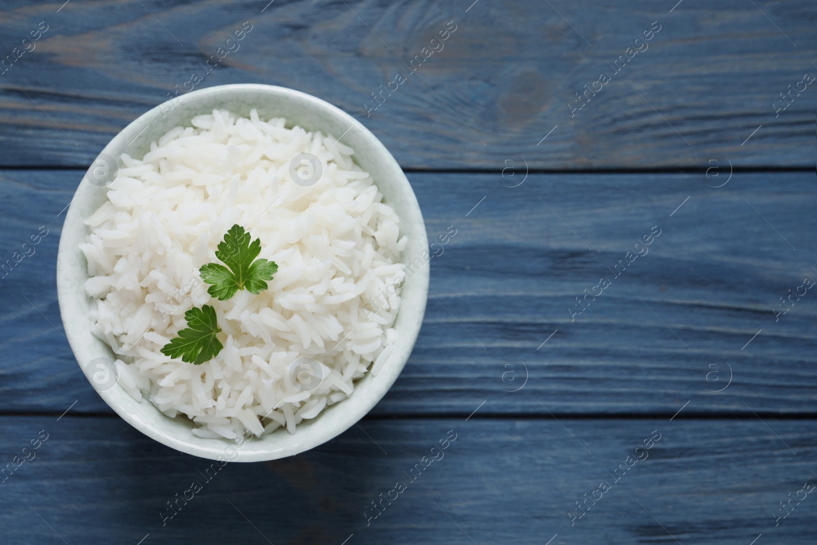 Photo of Bowl of cooked rice with parsley on wooden background, top view. Space for text