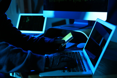 Hacker with credit card and laptop in dark room, closeup. Cyber crime