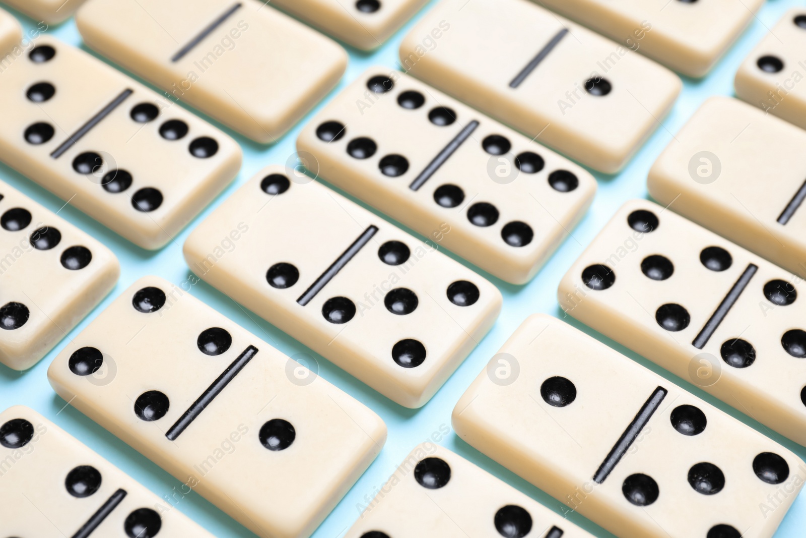 Photo of Set of classic domino tiles on light blue background, closeup