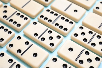Photo of Set of classic domino tiles on light blue background, closeup