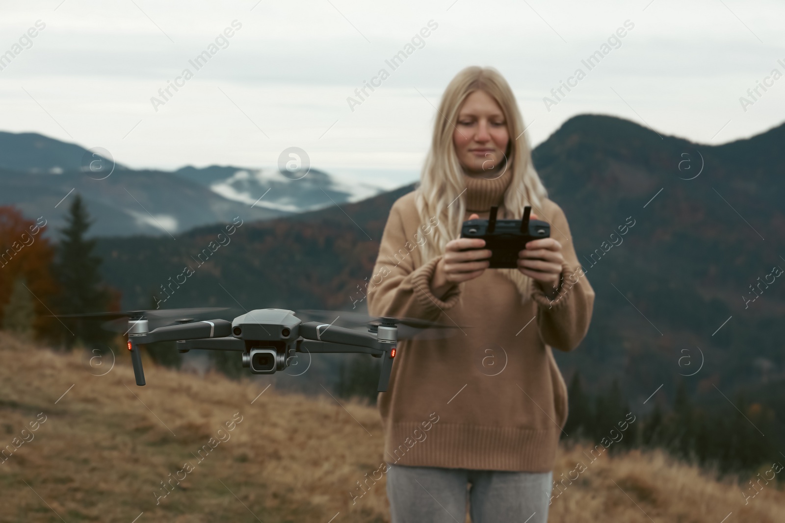 Photo of Young woman operating modern drone with remote control in mountains
