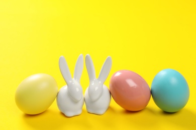 Ceramic Easter bunnies and dyed eggs on color background