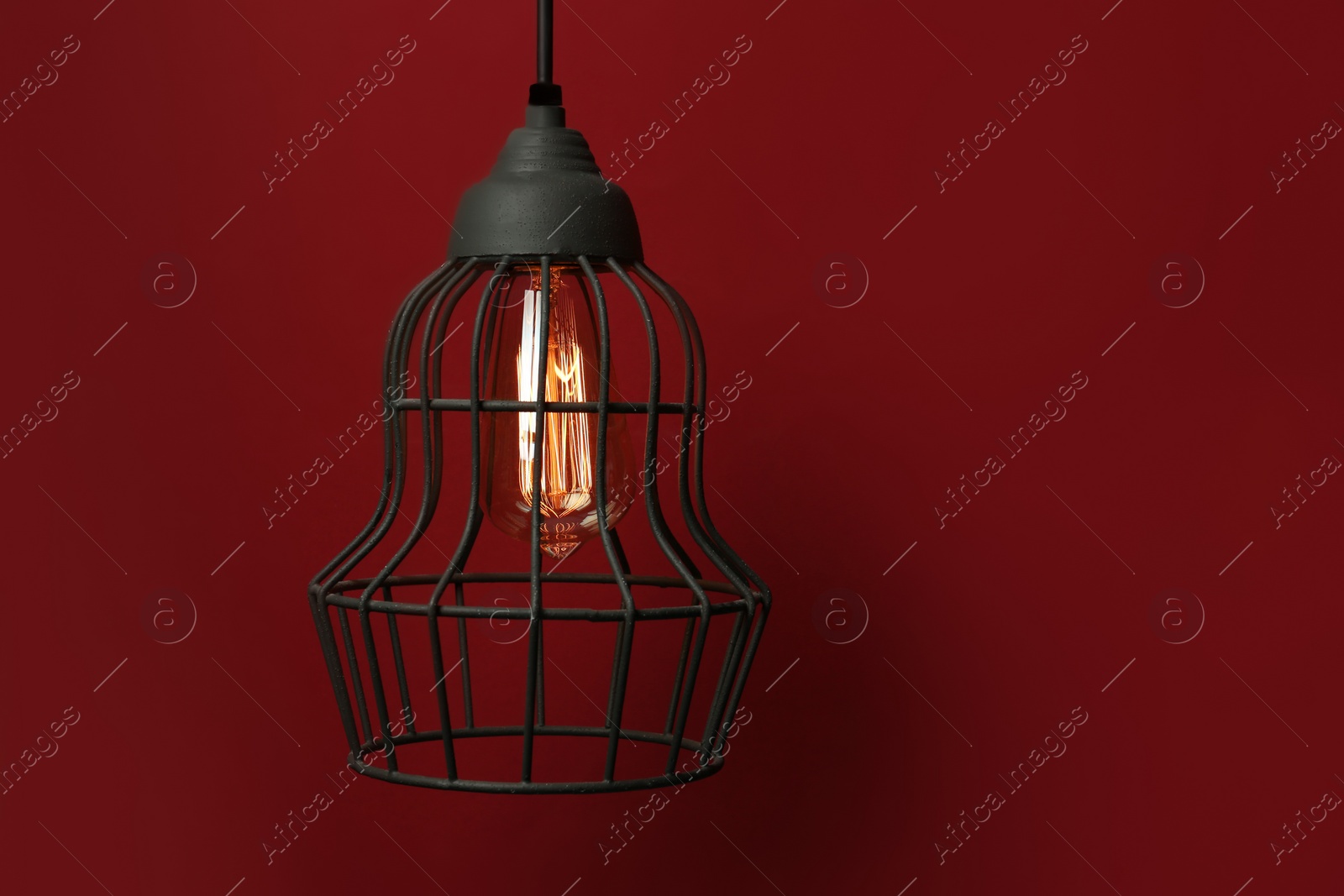 Photo of Hanging lamp bulb in chandelier against dark red background, space for text