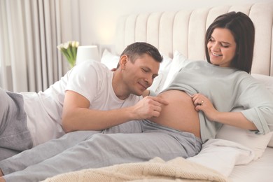 Photo of Young pregnant woman with her husband in bedroom