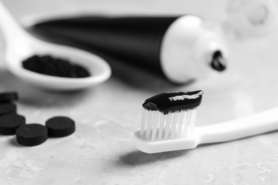 Photo of Brush with charcoal toothpaste on light grey table, closeup