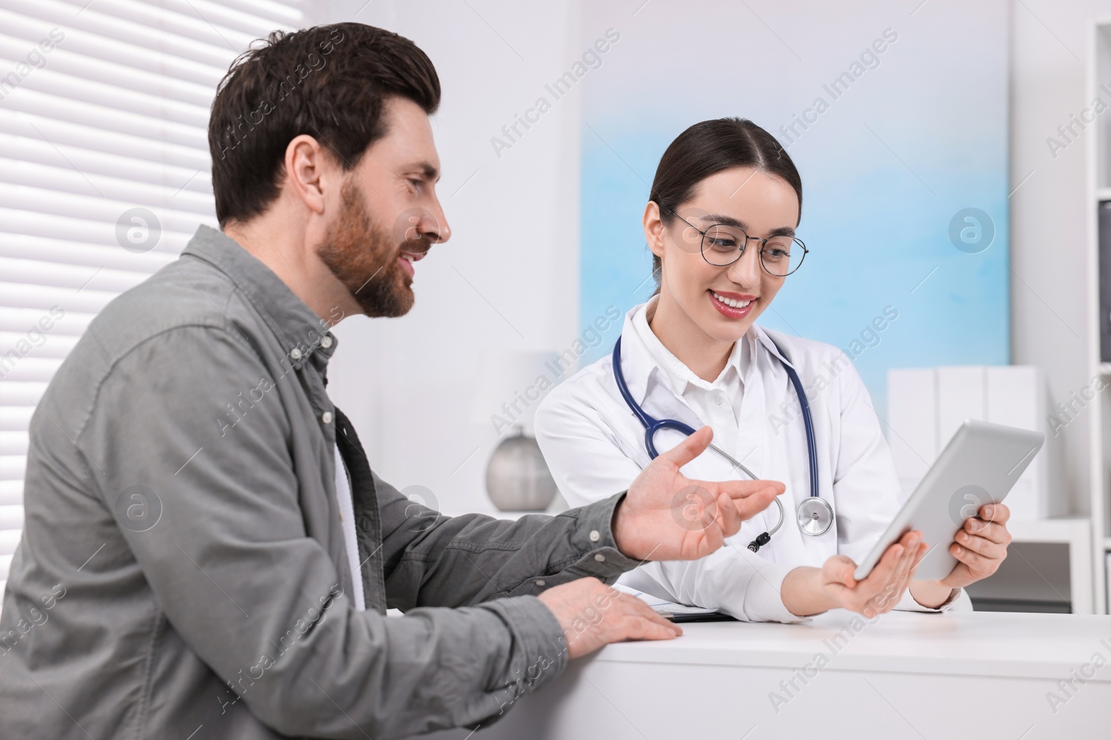 Photo of Doctor with tablet consulting patient during appointment in clinic