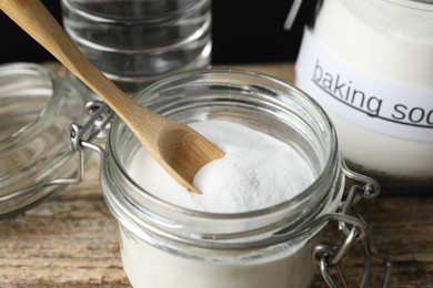 Photo of Baking soda, spoon and vinegar on wooden table, closeup