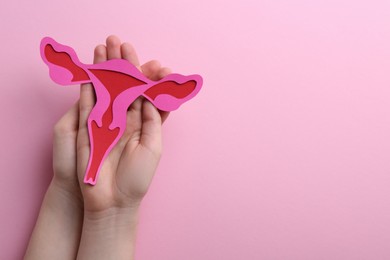 Photo of Reproductive medicine. Woman holding paper uterus on pink background, top view with space for text