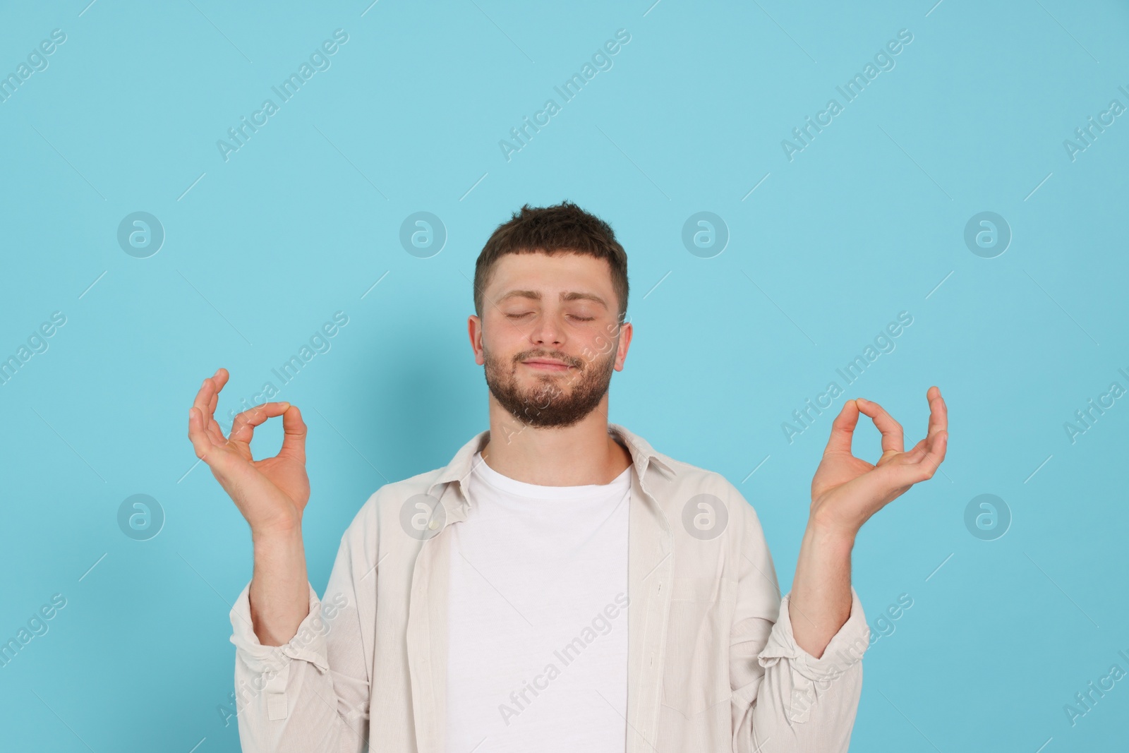 Photo of Young man meditating on light blue background. Zen concept