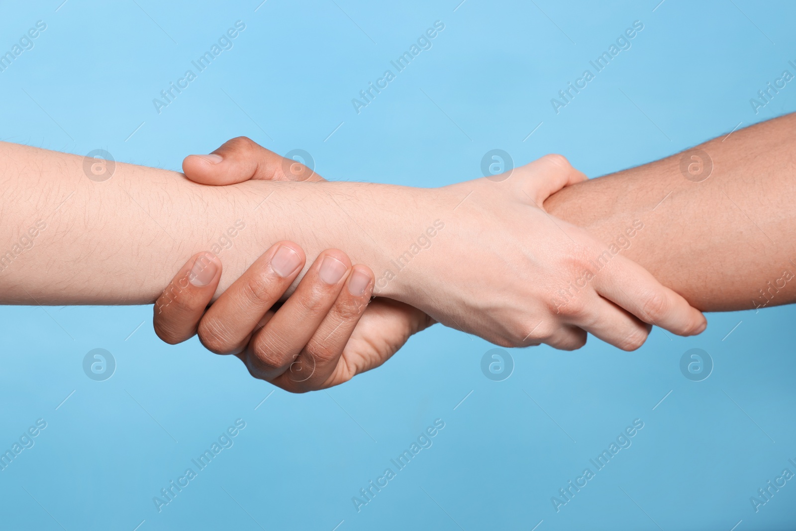 Photo of International relationships. People holding hands on light blue background, closeup