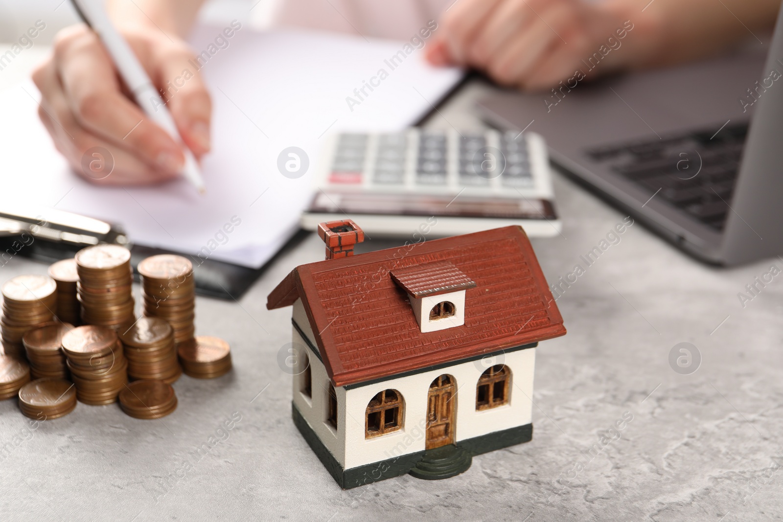 Photo of Woman planning budget at grey table, focus on house model