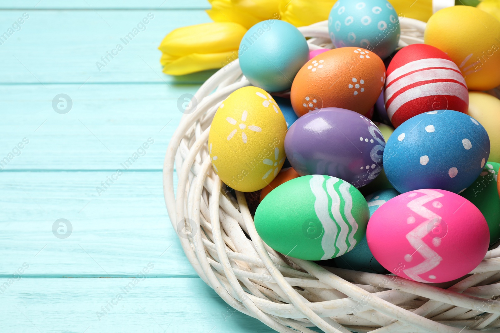 Photo of Colorful Easter eggs in decorative nest on light blue wooden background, closeup