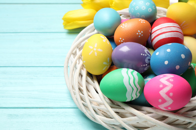 Colorful Easter eggs in decorative nest on light blue wooden background, closeup