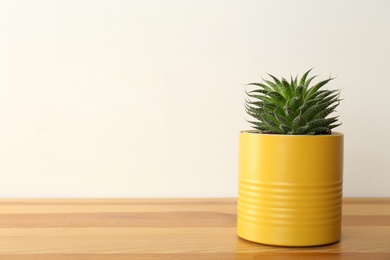 Photo of Houseplant in yellow tin can on wooden table, closeup. Space for text