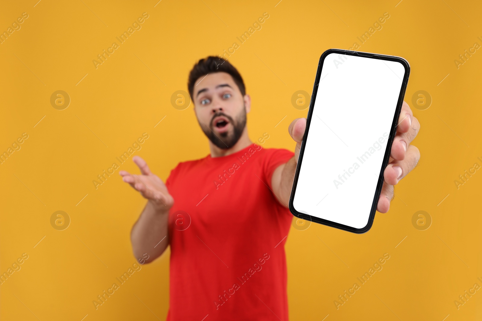 Photo of Surprised man showing smartphone in hand on yellow background, selective focus. Mockup for design