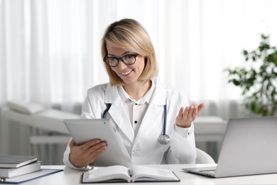 Smiling doctor with tablet having online consultation at table in office