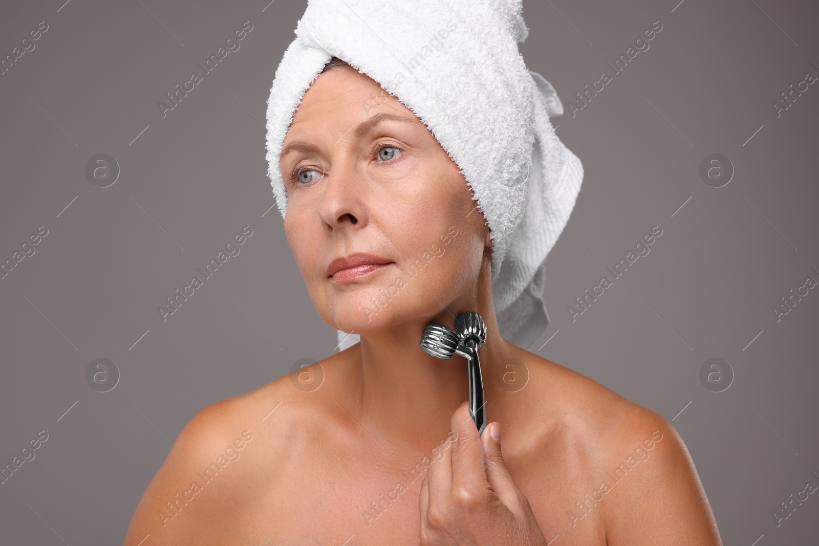 Photo of Woman massaging her face with metal roller on grey background