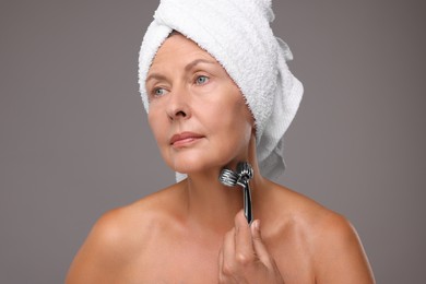 Woman massaging her face with metal roller on grey background