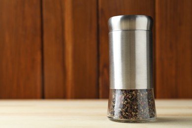 Photo of Pepper shaker on light wooden table, closeup. Space for text