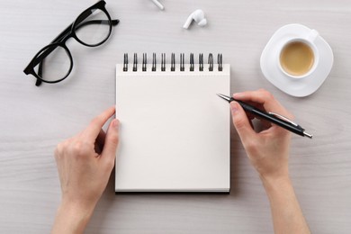 Woman with notebook and pen at white wooden table, top view. Space for text