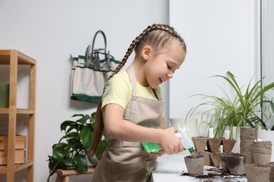 Little girl spraying water onto vegetable seeds in peat pots on window sill indoors