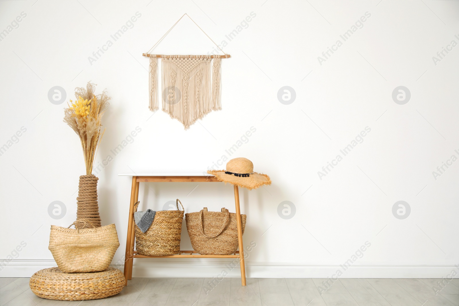 Photo of Stylish room with wooden table and wicker bags near white wall, space for text. Interior design