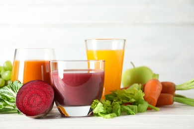 Glasses with different juices and fresh ingredients on table