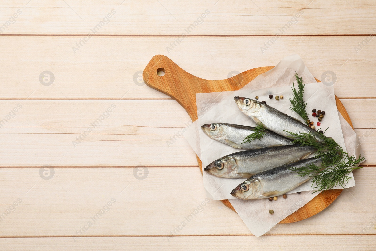 Photo of Fresh raw sprats, peppercorns and dill on light wooden table, top view. Space for text