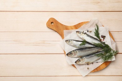 Photo of Fresh raw sprats, peppercorns and dill on light wooden table, top view. Space for text